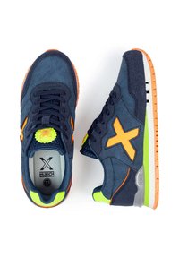 Zapatillas deportivas azul marino con acentos en naranja, tejido texturizado, detalles en verde lima y suela de goma. Presenta un logo circular en la lengüeta.