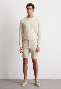 Pull en maille beige clair avec un col rond, associé à un short beige clair et des mocassins beiges. Design simple avec des détails côtelés.