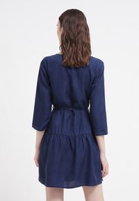 Abito blu navy realizzato in tessuto leggero, con vita aderente, maniche a tre quarti e orlo a volant a strati.