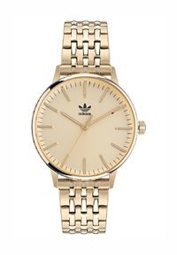 Montre-bracelet dorée avec un cadran beige, marqueurs d'heure fins et un bracelet en métal texturé. Comprend un logo à 12 heures et une couronne.