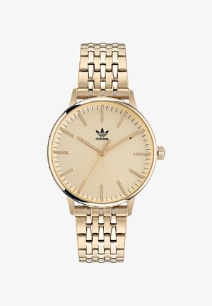 Gold-tone wristwatch with a beige dial, slim hour markers, and a textured metal bracelet. Features a logo at 12 o'clock and a crown.