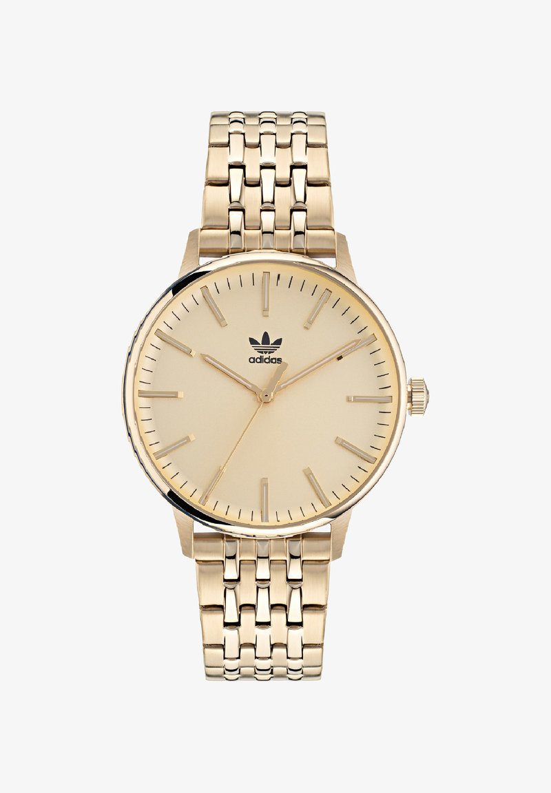 Kuldtooni randmeasi beežil dialiga, õhukeste tunni markeritega ja tekstuuriga metallist käevõru. Omab logosid kell 12 ja kroon.