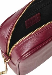 Borsa in pelle borgogna con finitura testurizzata, zip dorata e tracolla a catena. L'interno presenta una fodera nera e un'etichetta in pelle con il marchio.