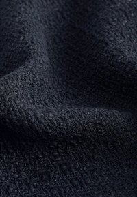 Gros plan sur un tissu bleu marine foncé texturé avec un motif tissé légèrement en relief et une surface douce et duveteuse.
