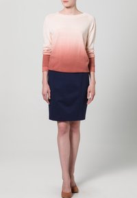 Un pull ombré léger passant de la crème au corail, associé à une jupe crayon marine et des escarpins beiges, créant un look décontracté superposé.