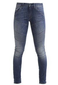 Jeans de denim ajustados en azul oscuro, con textura acanalada en las rodillas, cinco bolsillos y cierre de botón. Detalle de dobladillo sin terminar.