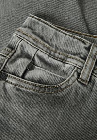 Pilkas džinsinio audinio audinys su kišeniu, pasižymintis kontrastingomis siūlėmis ir mažomis juodomis sagutėmis. Paviršius atrodo minkštas su nedideliu blizgesiu.