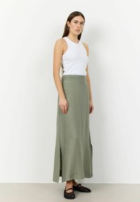 Top sin mangas blanco acanalado combinado con una falda larga de color verde oliva que presenta detalles de abertura. La modelo lleva puestos unos zapatos de esparto negros. Diseño simple y discreto.