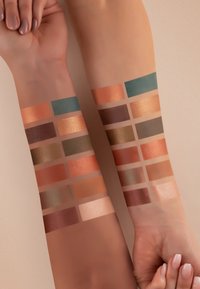 Farbproben von 12 Lidschatten-Nuancen auf Armen, die metallische und matte Finishes in Orange-, Braun-, Türkis- und Nude-Tönen zeigen, angeordnet in Rechtecken.