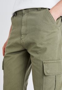 Olívazöld pamut cargo nadrág sima textúrával, oldalsó zsebekkel és megerősített varrással az illesztések mentén.