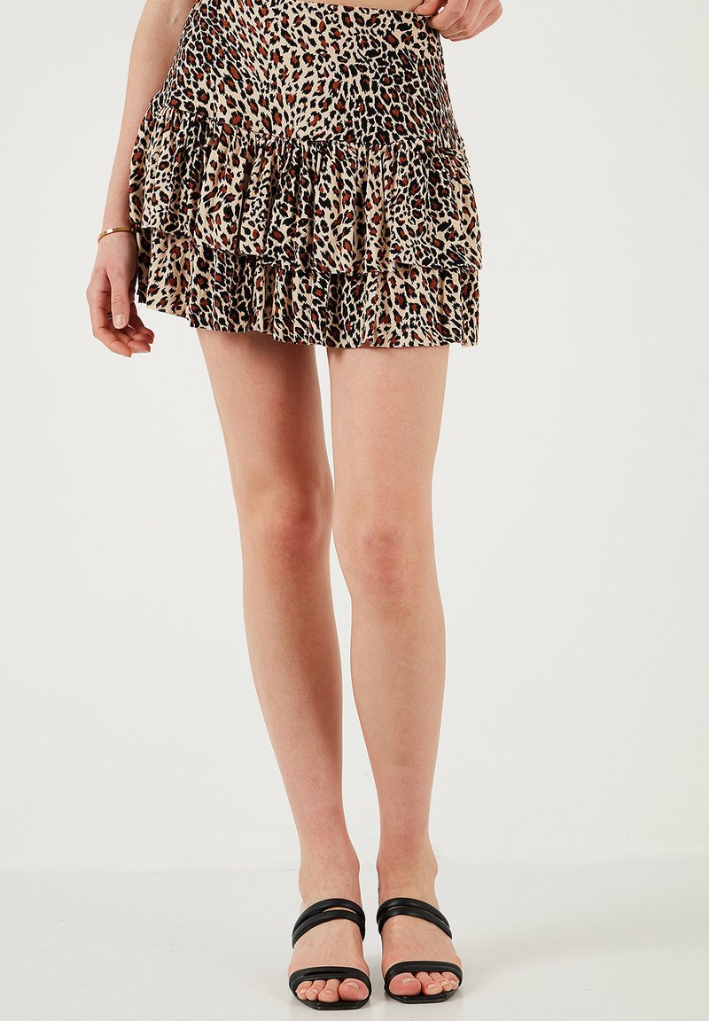 Mini gonna in stampa leopardata realizzata in tessuto leggero, con balze arricciate, vita aderente e uno sfondo beige con macchie nere e arancioni.