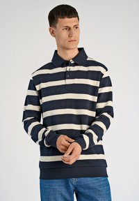Granatowo-kremowa koszulka polo w paski z długimi rękawami, kołnierzykiem na guziki i ściągaczami przy rękawach. Wykonana z miękkiego materiału bawełnianego o mieszanym składzie.