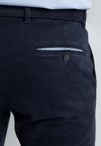Marineblauwe katoenen broek met een zachte textuur, voorzien van een achterzak met een knoop en een lichtblauwe bies langs de opening.