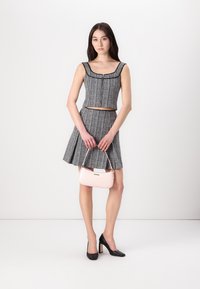 Ensemble de crop top en tweed noir et blanc avec une jupe évasée, associé à un sac à main rose clair. Le mannequin porte des talons hauts noirs.