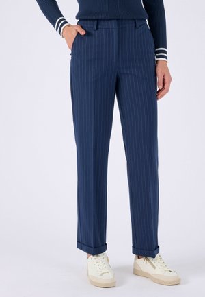 Marineblauwe pantalon met krijtstreep en omgeslagen zomen, gedragen met witte sneakers en een marineblauwe geribbelde trui met gestreepte manchetten.