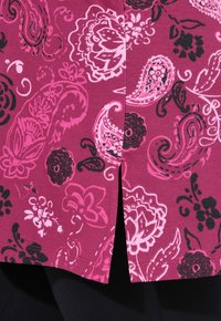 Korte mouwen top met een bordeauxrode basis, versierd met roze en zwarte bloemen- en paisleypatronen, en een zijsplit voor extra detail.