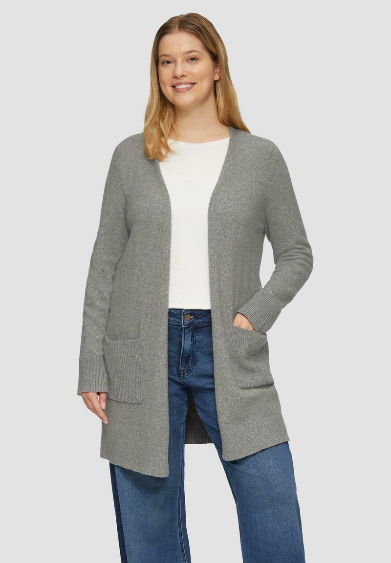 Grijze cardigan met lange mouwen, open voorkant, geribbelde zoom en twee voorzakken, gedragen over een witte top en blauwe jeans. Zachte textuur.