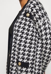 Zwart-wit houndstooth patroon cardigan met gouden knoopaccenten, met een relaxte pasvorm en zijzakken. Gemaakt van brei-materiaal.