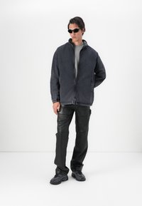 Casaco de denim preto com fecho éclair e colarinho alto, combinado com calças de couro pretas ajustadas e ténis pretos elegantes. Apresenta um design minimalista.