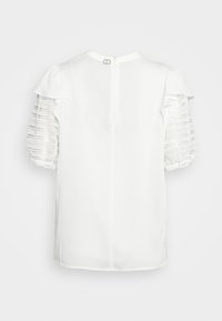 Blusa bianca con maniche puff trasparenti e testurizzate con dettagli in pizzo, scollatura rotonda e chiusura a bottoni sul retro.