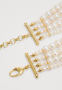Mehrsträngiges Perlenarmband mit goldenen Beschlägen. Unregelmäßige weiße und cremefarbene Perlen sind auf einer goldenen Kette aufgezogen und verfügen über einen Karabinerverschluss.