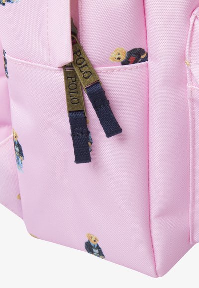 Sac à dos rose texturé arborant de petits graphiques d'ours, agrémenté de zips navy étiquetés "POLO". Tissu durable avec une finition lisse.