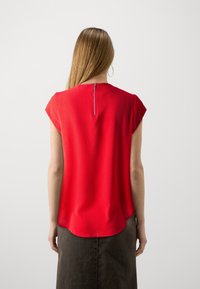 Rote Bluse mit kurzen Ärmeln aus leichtem Stoff, mit abgerundetem Saum und einem Reißverschluss auf der Rückseite für müheloses An- und Ausziehen.
