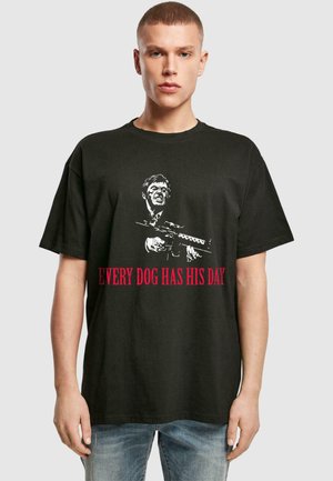 Svart bomull T-skjorte med et grafisk bilde av en mann med et våpen og teksten "HVER HUND HAR SIN DAG" i fet rød. Korte ermer, avslappet passform.