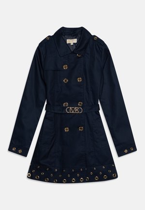 Navy double-breasted trench coat with gold buttons, a belted waist, and grommet detailing at the hem. Made from a smooth fabric.