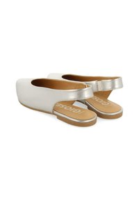 Chaussures slingback blanches avec une sangle argentée métallique et une semelle intérieure beige. Semelle plate, texture lisse et design à bout rond. Nom de la marque visible à l'intérieur.