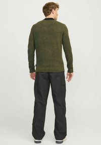 Olive green knitted sweater with long sleeves, textured finish, and black collar, paired with black cargo pants featuring multiple pockets.