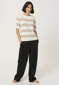 Kremno belo majico s kratkimi rokavi v črtah, kombinirana s črnimi hlačami sproščenega kroja. Obutev ima svetel podplat in preprost dizajn.