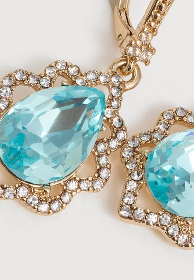 Χρυσά σκουλαρίκια με μεγάλα μπλε πετράδια σε σχήμα σταγόνας, περιβαλλόμενα από μικρά καθαρά κρυσταλλάκια σε περίτεχνες βάσεις.