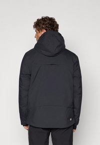Schwarze Atempufferjacke mit Kapuze, ausgestattet mit einer glatten Textur, einem Reißverschluss vorne und elastischen Manschetten. Auffälliges Design des Rückenteils.