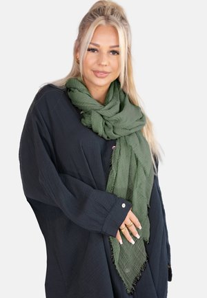 Green textured scarf made of lightweight fabric, draped neatly around the neck. Worn over a dark long-sleeve shirt with visible buttons.