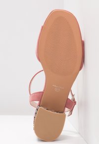 Sandale en daim rose avec une semelle plate en caoutchouc texturé, une sangle réglable et un détail tissé décoratif au niveau du talon. Taille 37.