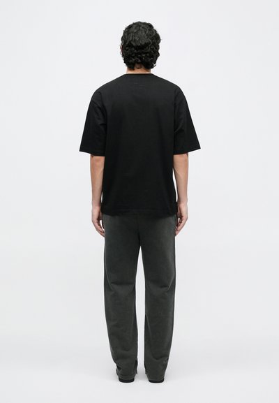 Black short-sleeve t-shirt made of cotton, with a crew neckline and relaxed fit. Worn with gray pants, viewed from the back. Plain design.