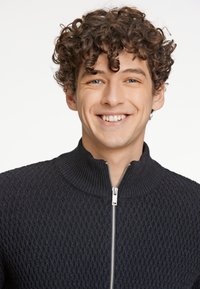 Chaqueta azul oscuro con cremallera, que presenta un patrón de diamante texturizado y un cuello alto con un detalle de cremallera plateada.