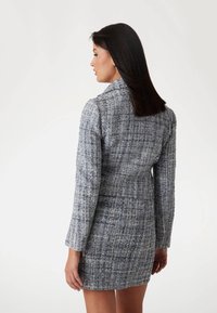 Harmaa tweed mini-mekko, jossa on teksturoitu kangas, pitkät hihat ja kaulus. Mukana istuva malli ja paljaat vetoketjulevyt hiiroilla.