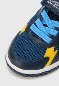 Μπλε και κίτρινο αθλητικό παπούτσι με υλικό διχτυού, υφασμένα δερμάτινα στοιχεία και σόλα με σχέδιο. Οι κορδόνια είναι ανοιχτό μπλε.