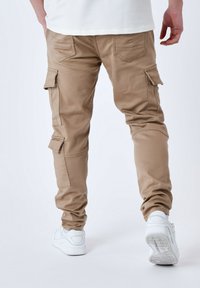 Pantaloni cargo color khaki con tasche laterali e gambe affusolate, realizzati in tessuto resistente. Indossati con sneaker bianche.