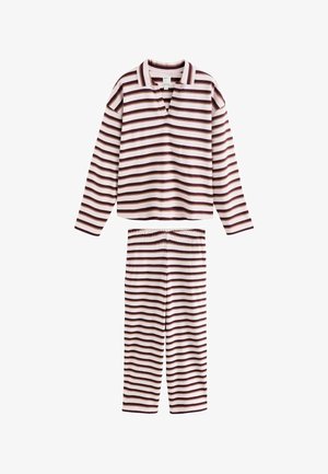 Jeune femme aux cheveux bruns mi-longs porte une chemise blanche à rayures horizontales marron et beige, debout devant un fond clair uni.