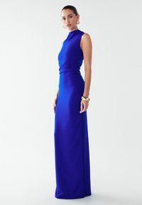 Modra oprijeta večerna obleka z visokim ovratnikom in bočnim nabiranjem, izdelana iz gladkega, raztegljivega materiala, dolga do tal s elegantno silhueto.