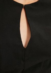 Černé šaty s výstřihem ve tvaru klíčové dírky a hladkým povrchem. Detailní pohled odhaluje minimalistický design s čistými liniemi a jemným prošíváním.