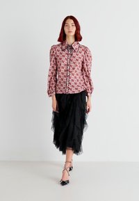 Camicia a fiori rosa con maniche a sbuffo, abbinata a una gonna di tulle nera a strati e tacchi neri con borchie. Look elegante e ricco di texture.