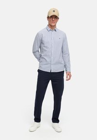 Gestreept button-up shirt in blauw en wit katoen, gecombineerd met navy broek en witte sneakers. Beigen pet met een logoaccent.