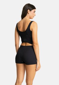 Débardeur noir à côtes avec un détail twist au dos, associé à un short à côtes assorti. Le tissu a une texture douce et extensible.