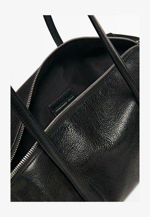 Czarna skórzana torebka z częściowo otwartym srebrnym zamkiem błyskawicznym, ukazującym czarną materiałową wyściółkę i wewnętrzną metkę z logo marki.