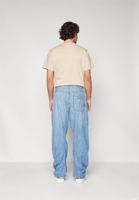 Bež majica s kratkimi rokavi in svetlo modri ohlapni jeans hlače, oboje sproščeno. Hlače imajo zadnje žepe in ravno silhueto.