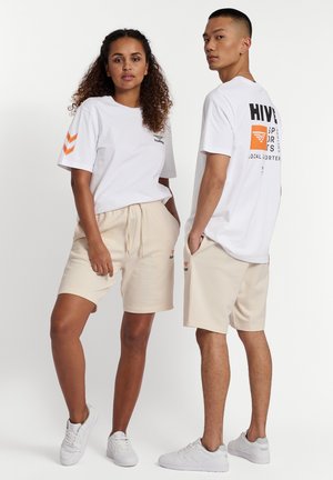Twee modellen staan tegen een witte achtergrond en dragen bijpassende witte grafische t-shirts en beige korte broeken met witte sneakers.